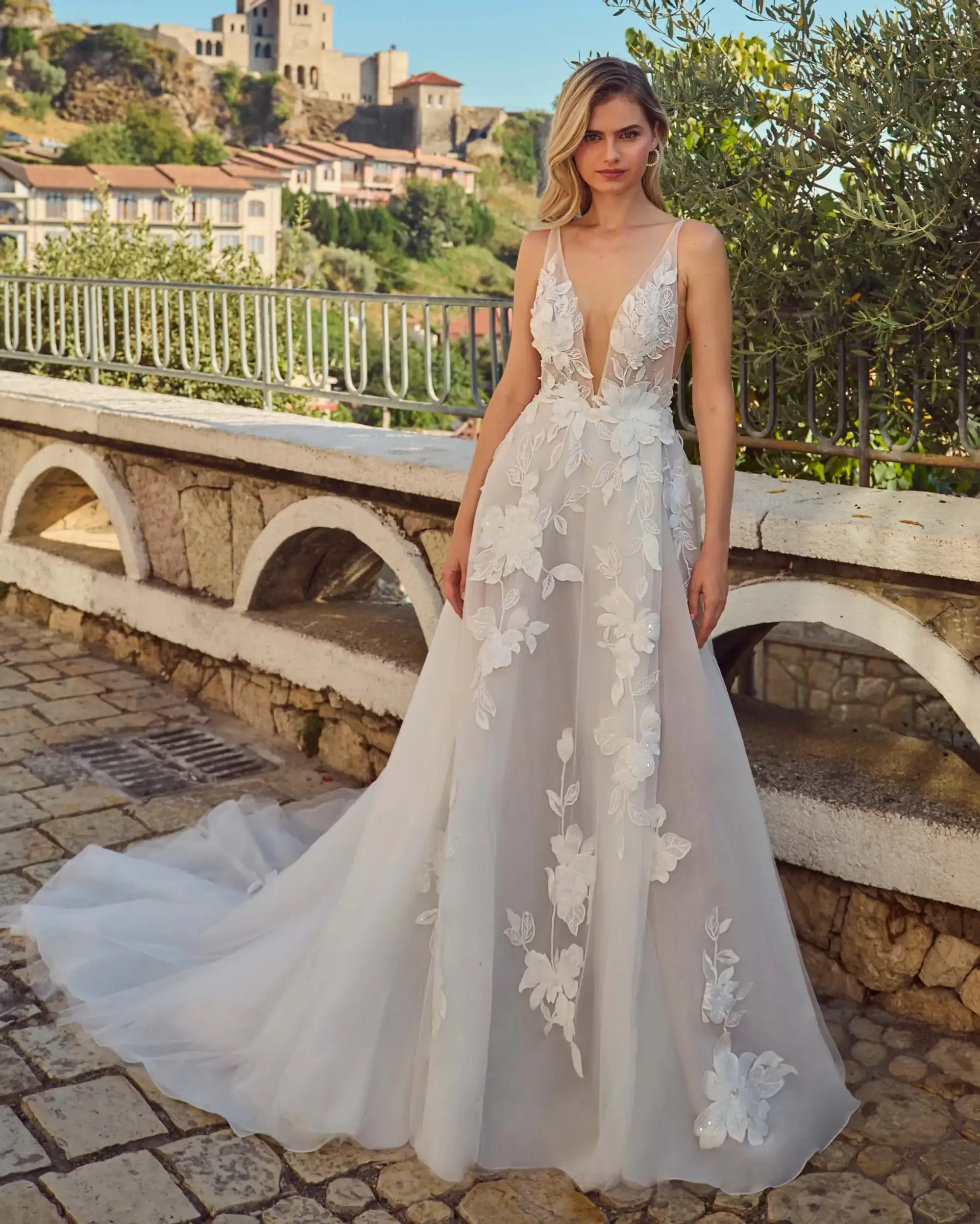 Model is wearing a sleeveless A-line wedding gown with a plunging neckline and delicate floral embroidery.