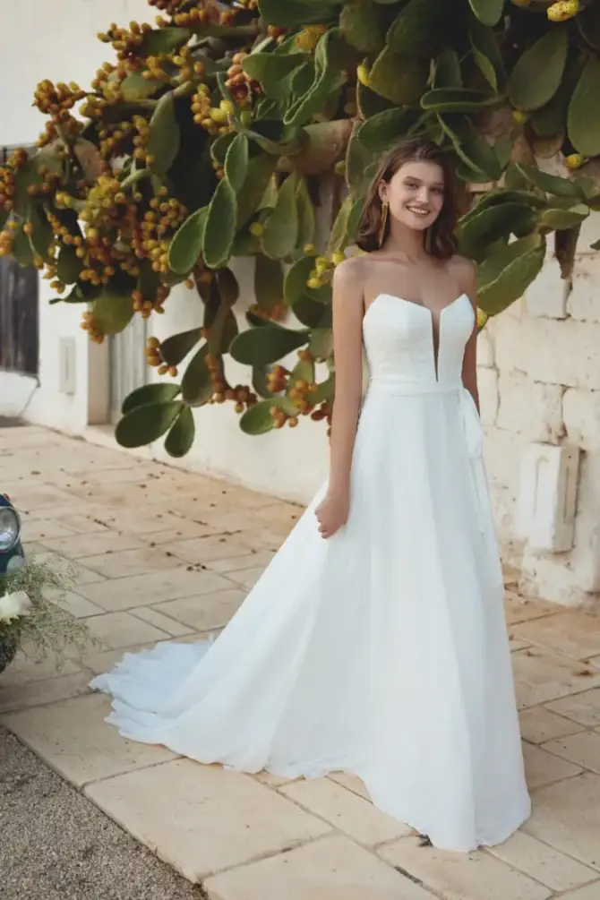 Model is wearing a strapless a-line wedding dress with a plunging neckline and train