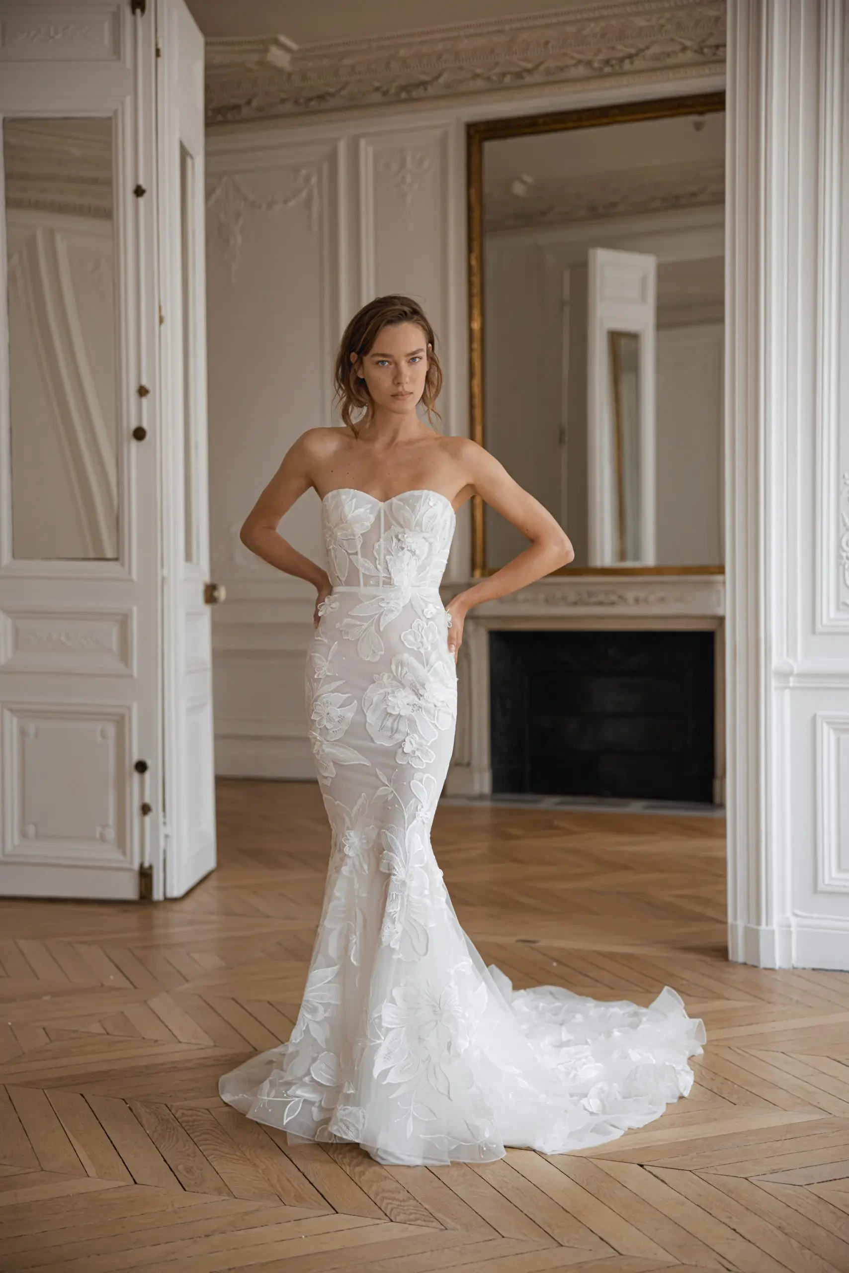 Model is wearing a strapless trumpet wedding gown made of detailed lace and a softly flared skirt.