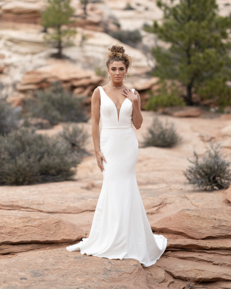 Model is wearing a sleek V-neck wedding dress made of soft crepe with a fitted, minimalist silhouette.