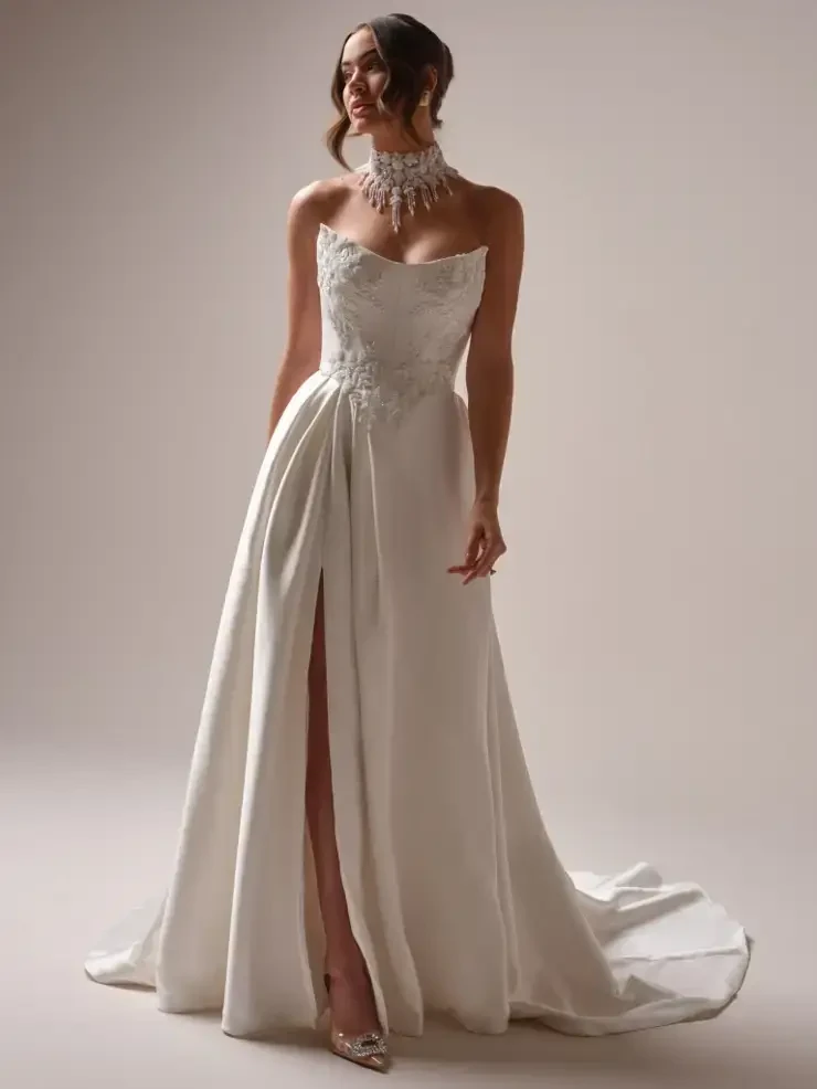 A woman in a strapless white dress with a high slit, wearing a statement necklace, posing elegantly.