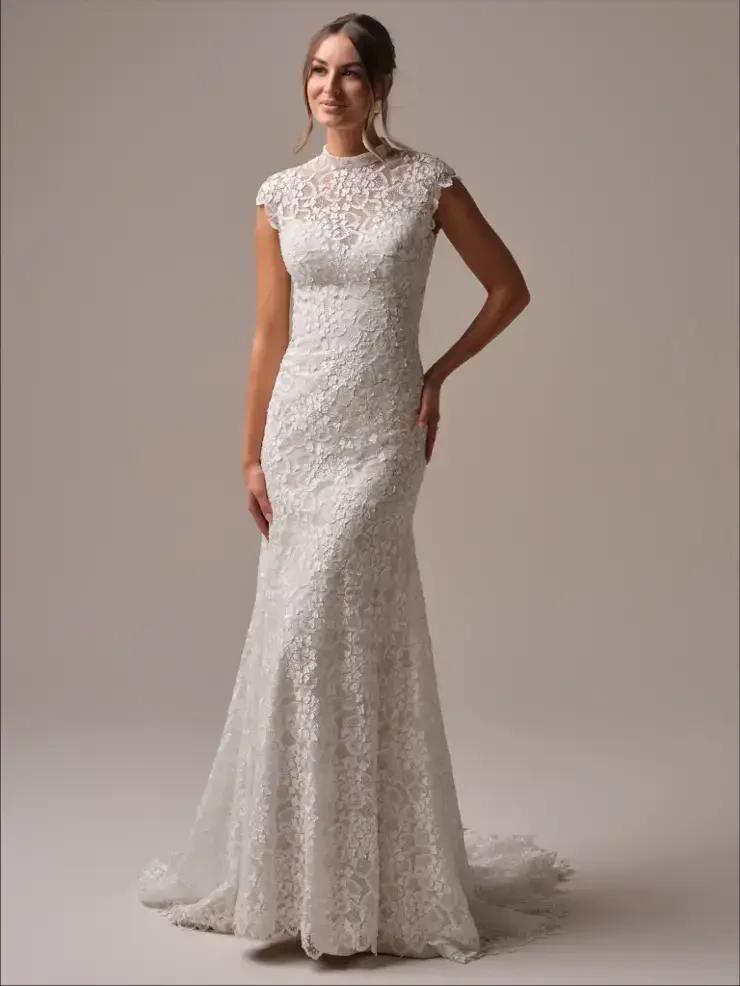 A model wearing a elegant white lace wedding dress with a fitted silhouette and cap sleeves, standing against a neutral background.