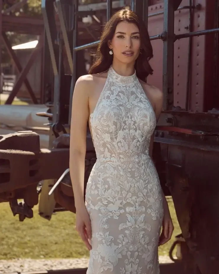 A woman in a sleeveless, intricately embroidered gown stands next to a train.